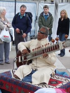 An Indian man playing sitar with audience gathered around him