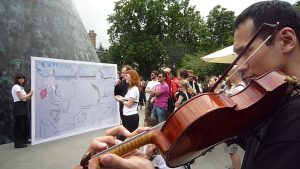 An Asian man playing viola with the cone in the background and audience gathered around.