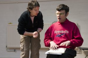 Andrew wearing glasses, sitting reading with Christine leaning over him on left with hands clasped