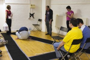 Audience member up on stage, bent over from the waist with cast and director and audience nearby