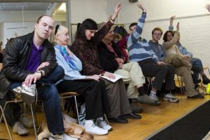 Front row of audience at the Oval House with four audience members raising a hand in the air