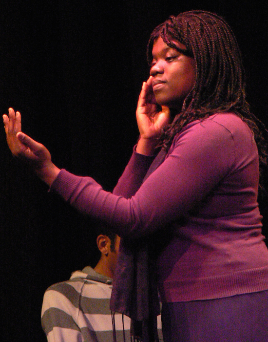 A close up of a black female actor ‘fixing her face’ with an imagery mirror in her left hand.