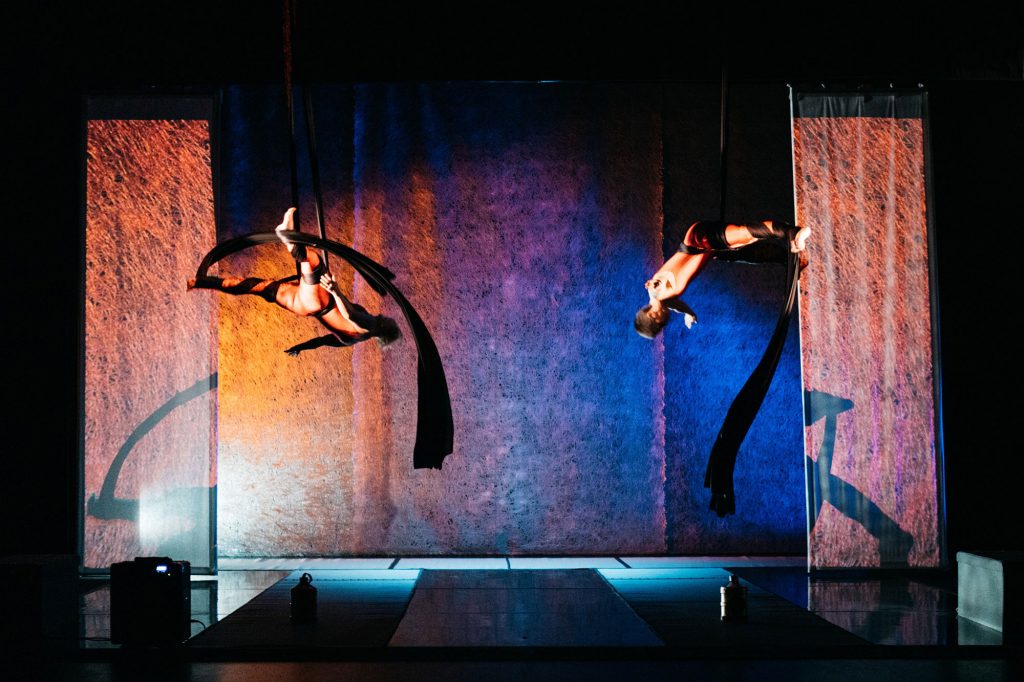 A wide landscape shot of two women on aerial silks mid-fall.