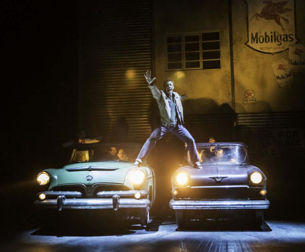 A man stands on top of two retro cars