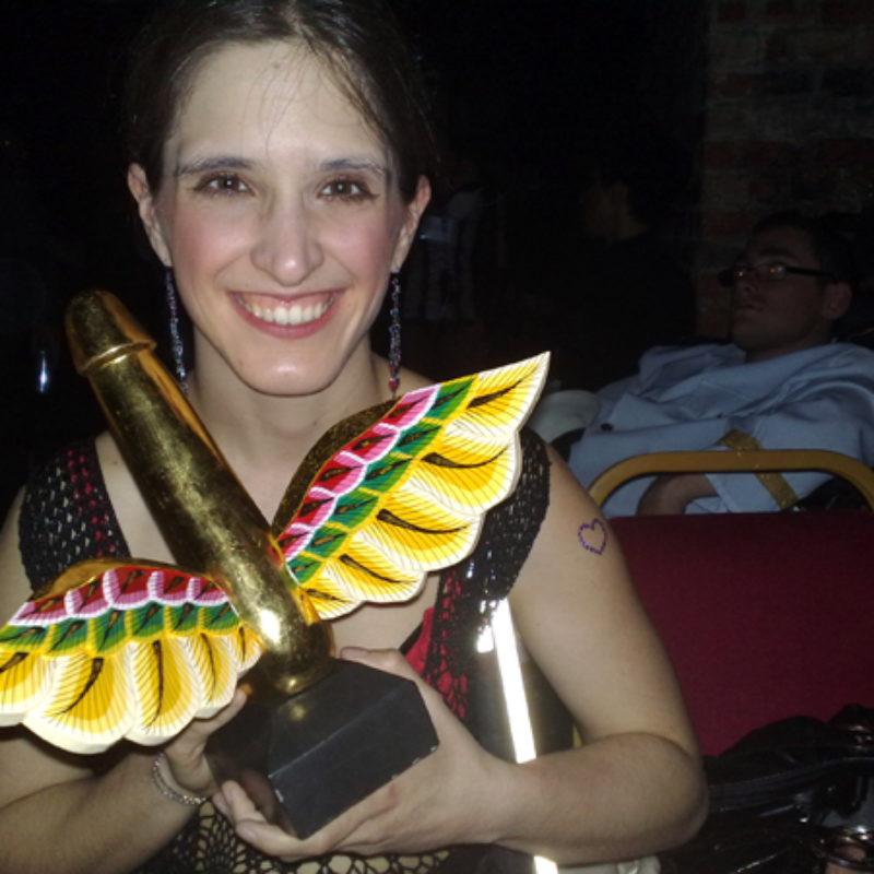 Amelia smiling - holds a gold winged phallus award