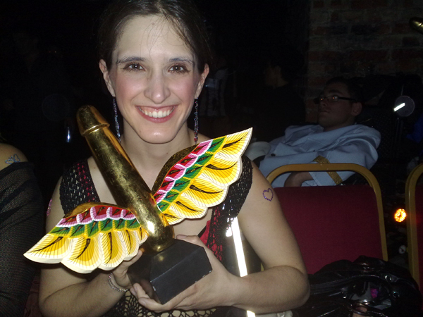 Amelia smiling - holds a gold winged phallus award