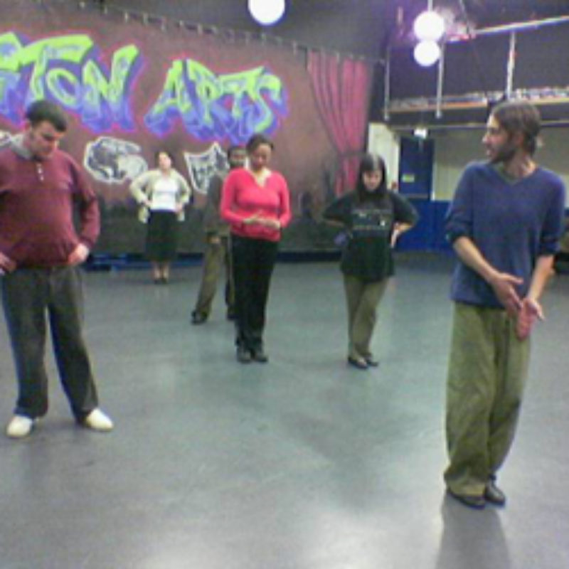A group of adult participants in a line behind a dance teacher in a studio. Film about a participation project