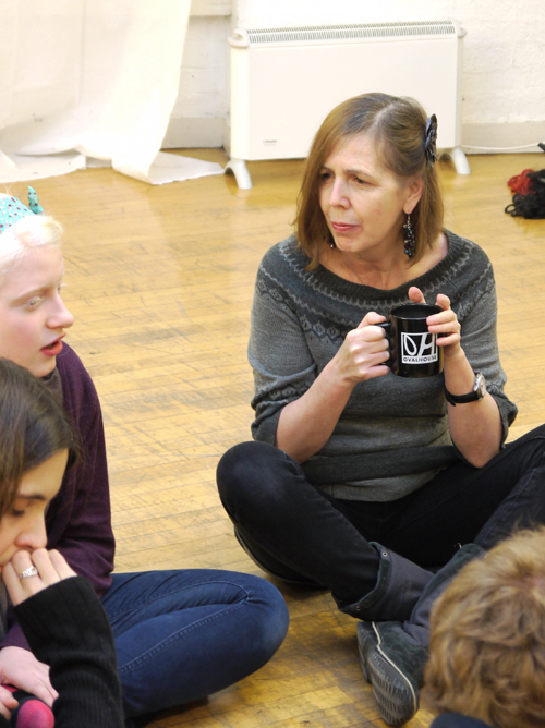 A close up shot of part of a group sitting in a circle deep in discussion. An older white actor has a mug of tea and is listening to the female actor sitting next to her.