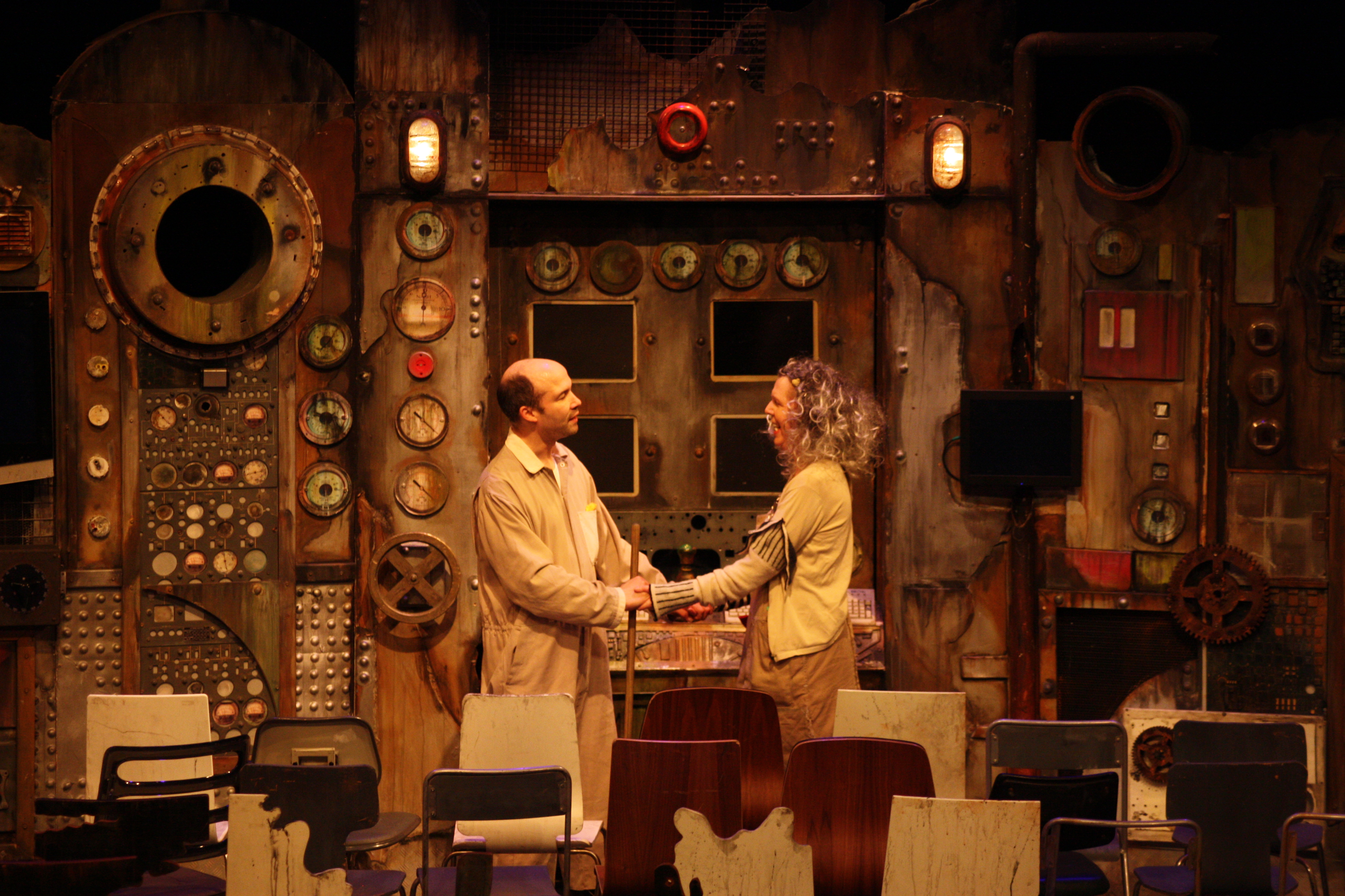 Tim as Old Man with Heather Gilmore as Old Woman in The Chairs. They stand behind the rows of chairs, holding hands as they celebrate the impending arrival of the Orator.