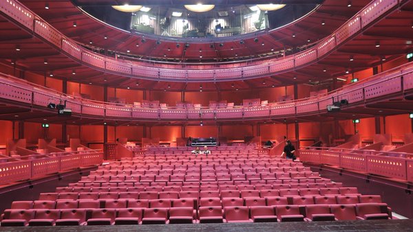 wide shot from the stage of the Lowry auditorium (venue for the Chairs); three levels of empty red seats with Artistic director Maria Oshodi