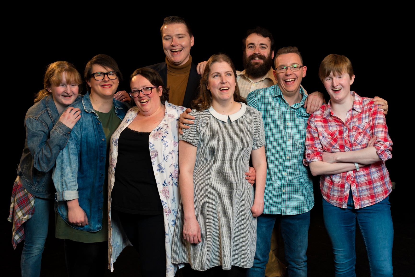 8 Pathways actors huddled in a group, hands relaxed on each others shoulders, all smiling, mid laughter