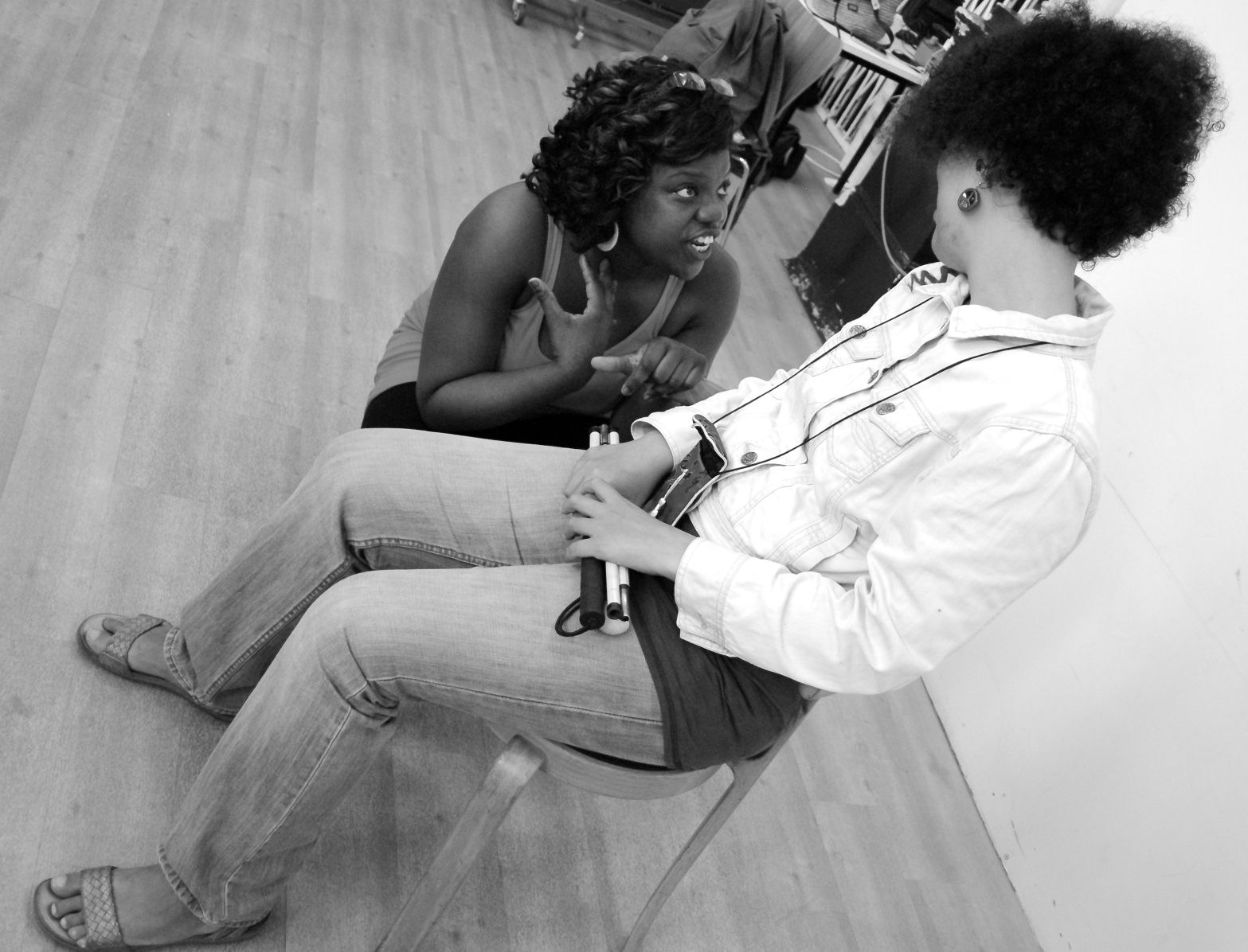 Anita, the assistant facilitator, squats down to talk to one of the participants who is seated looking down at her. Anita's face is animated as she gestures towards herself with one hand. Black and white picture