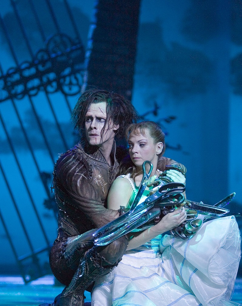 Male dancer dressed as Edward Scissorhands with blade-like fingers hugs a female dancer dressed in white