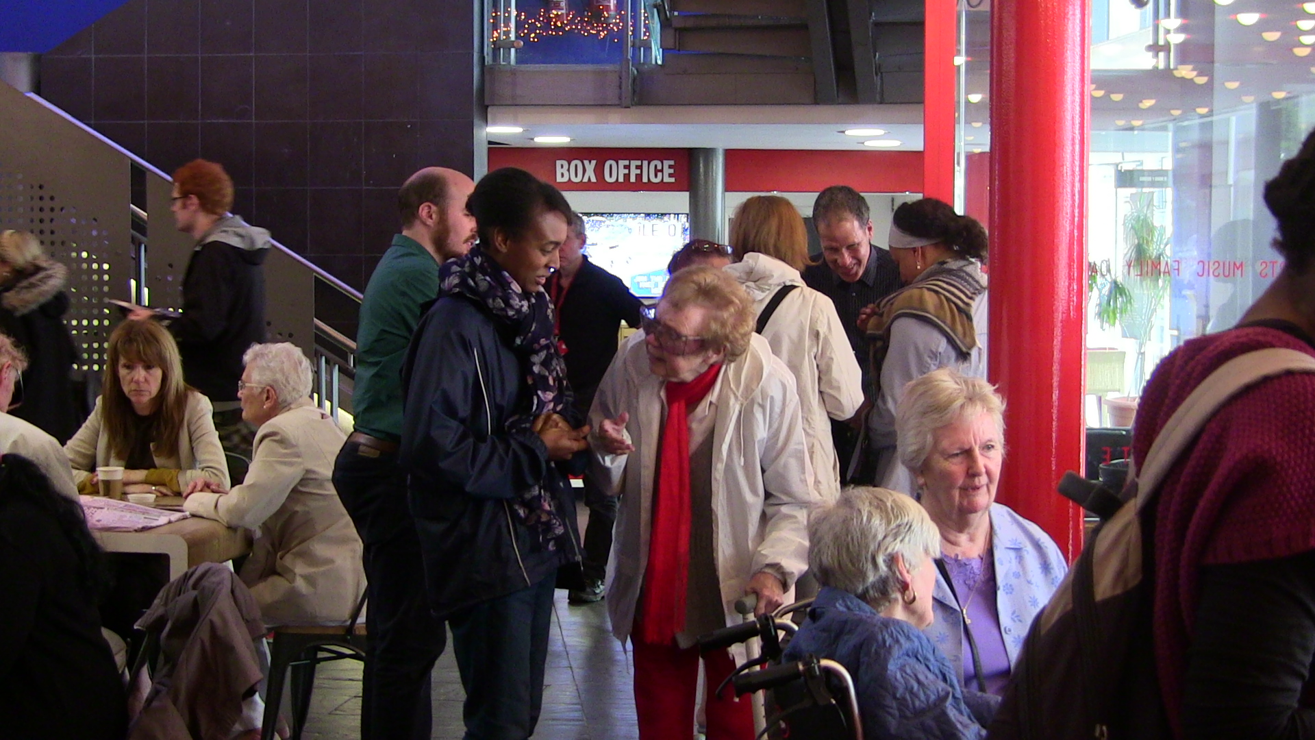 Various groups of people sitting and standing in the Stratford foyer. Centre: an older woman and access worker in covnersation.