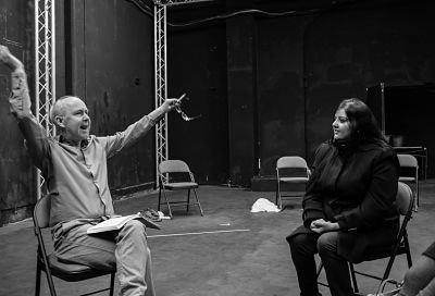 Director Shane Irwins gestures hands outwards while a youth theatre participant sat next to him listens on.