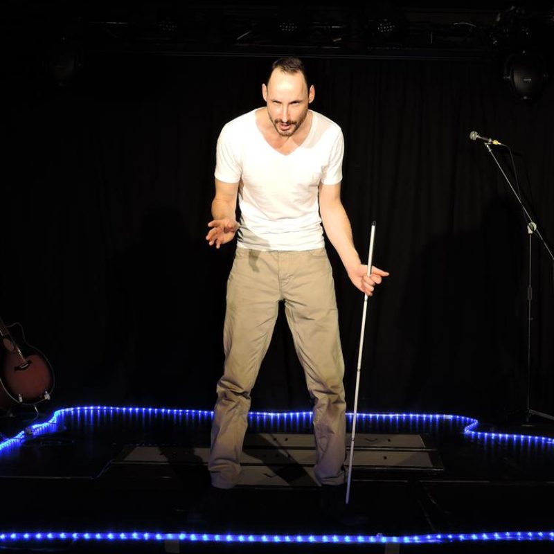 A white male performer stands centre stage