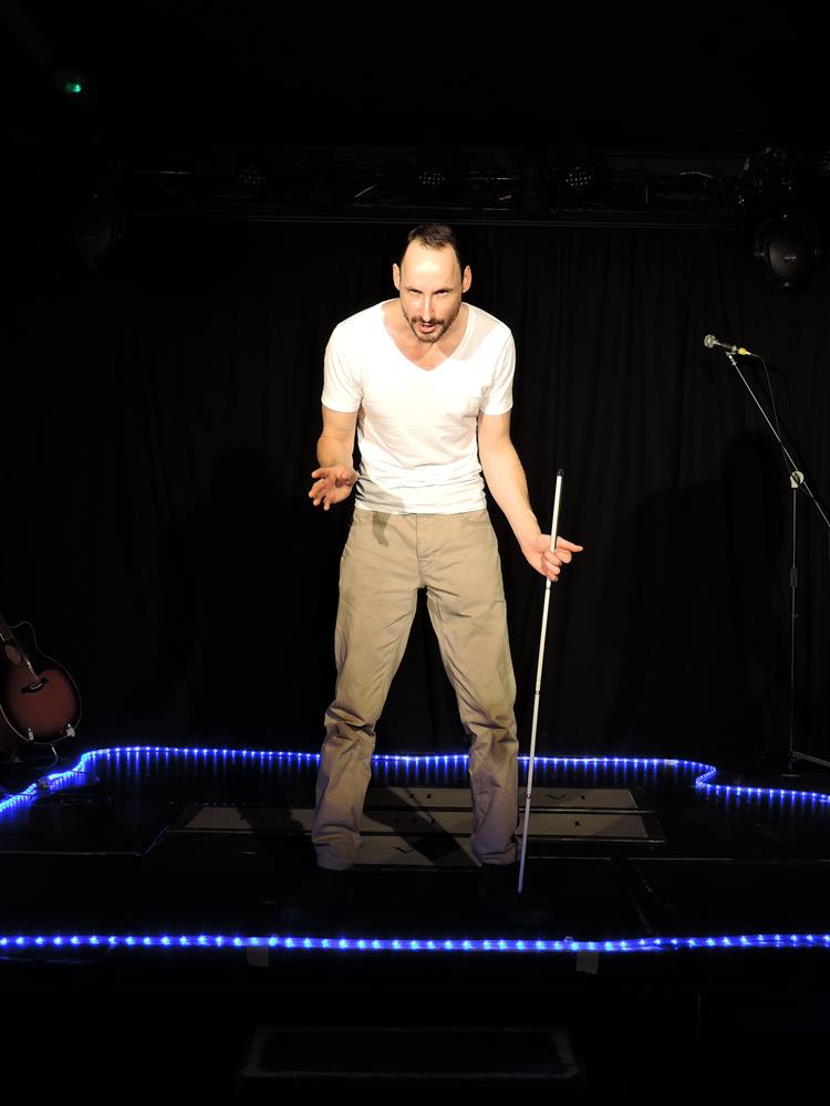 A white male performer stands centre stage