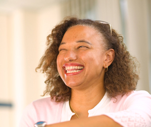A portrait image of Maria - a biracial woman wearing a pink top looking off to the right of the camera and laughing happily.