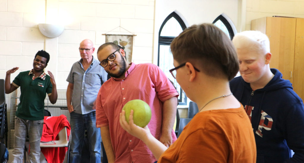 A group of young people in a brightly lit room giving a lot of attention to a grapefruit-sized ball.