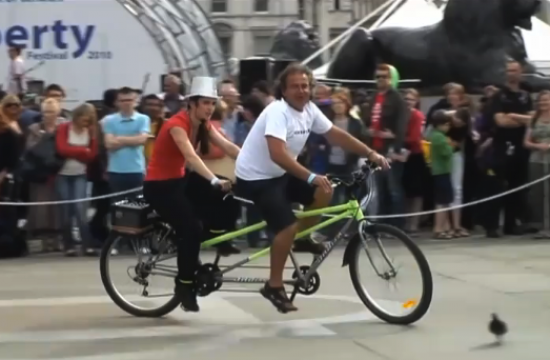 Two performers ride and sing on a tandem