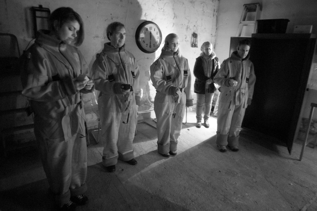 Flatland- A black and white shot of Two men and Two women standing in the dark. Dressed in neoprene boiler suits, they hold out haptic cubes in front of them which guide their way through the darkeness.