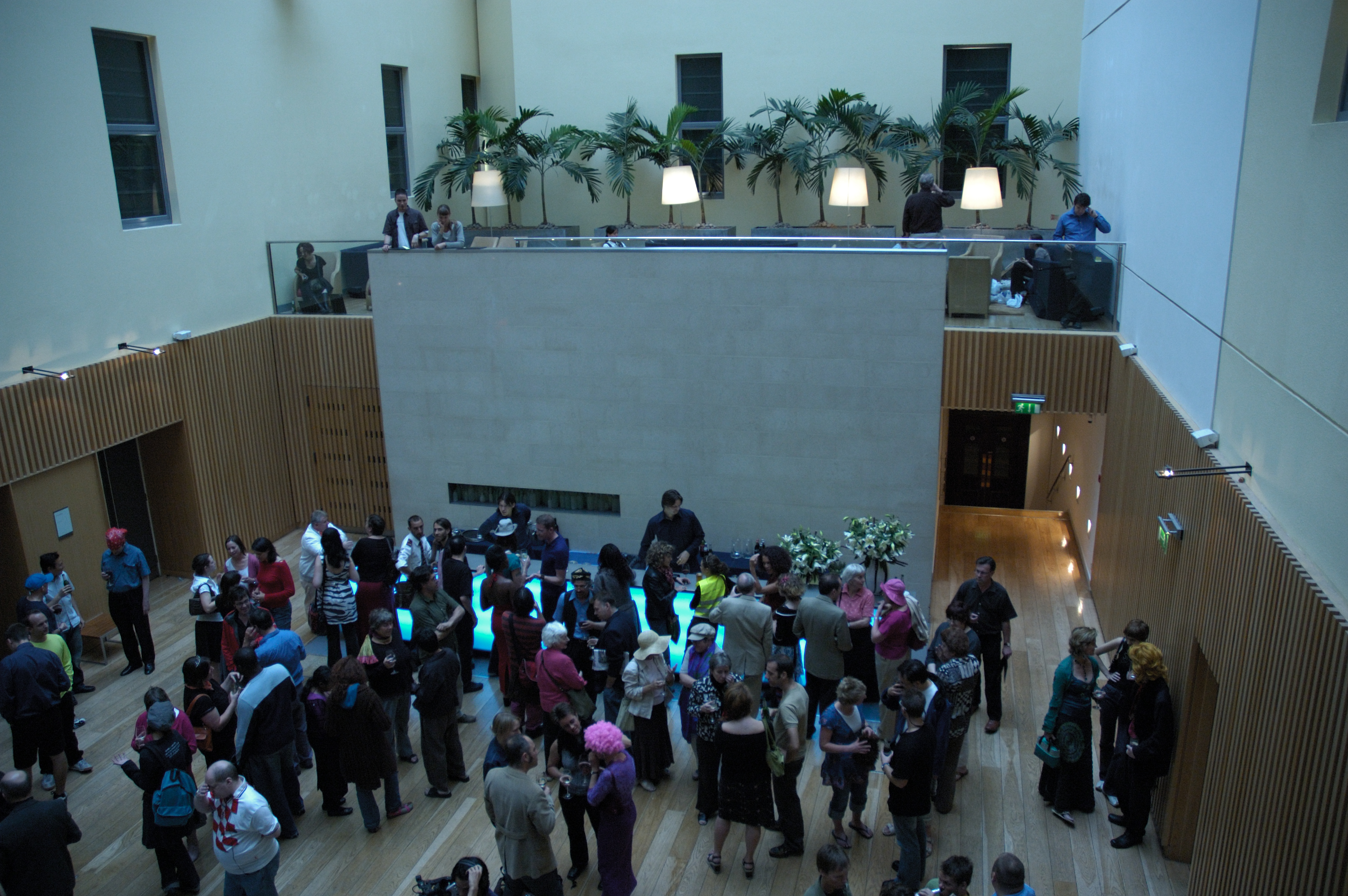From above, a large group of people on the party floor, drinking near a blue lit bar.