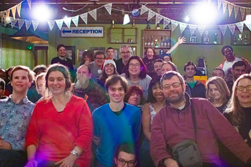 A group photo of the audience smiling from the perspective of the stage. A woman in the back has her hands up