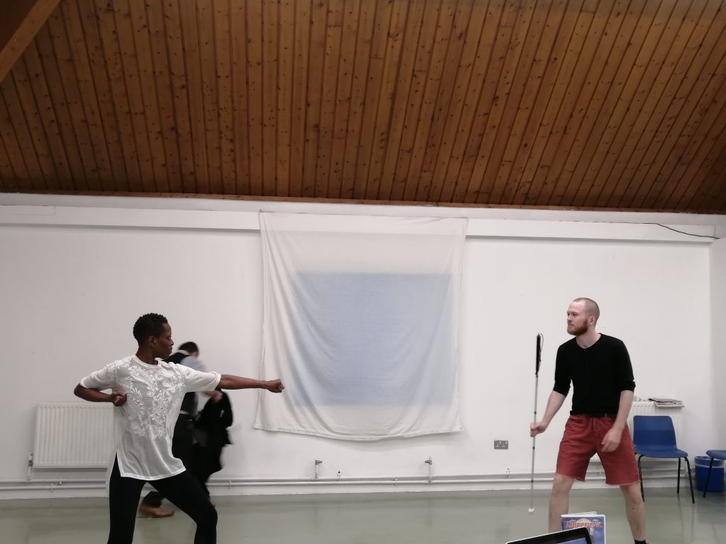 A Black woman motions with her arms in a fighter pose towards the young white man holding his cane ready for action