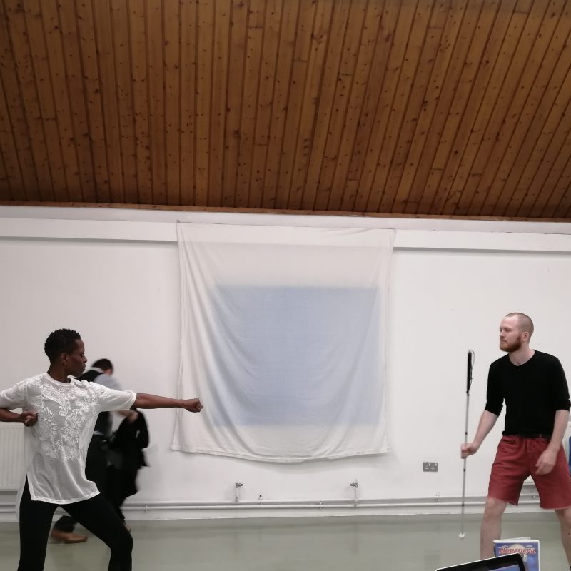 A Black woman motions with her arms in a fighter pose towards the young white man holding his cane ready for action