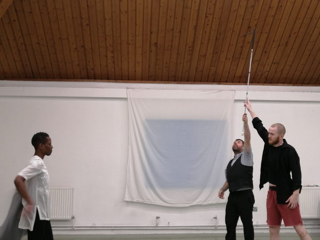 Two white men grasp a cane held high above their heads while a Black woman looks on