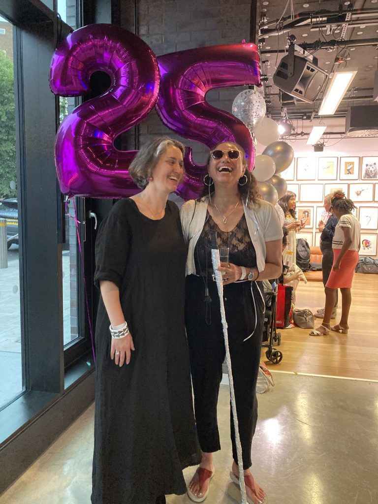 Mary Paterson and Maria Oshodi stand in front of two purple balloons, a 2 and a 5. They are both laughing. 