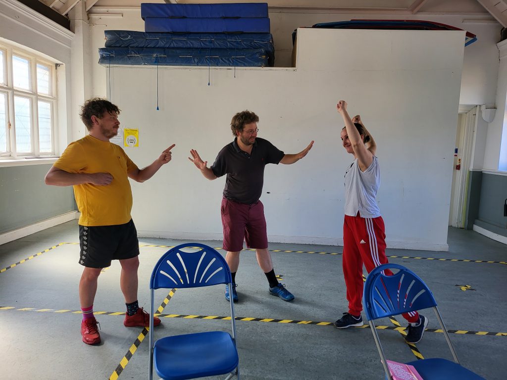 A group of three participants standing in a workshop space all posing in different ways. 