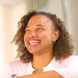 A portrait image of Maria - a biracial woman wearing a pink top looking off to the right of the camera and laughing happily.