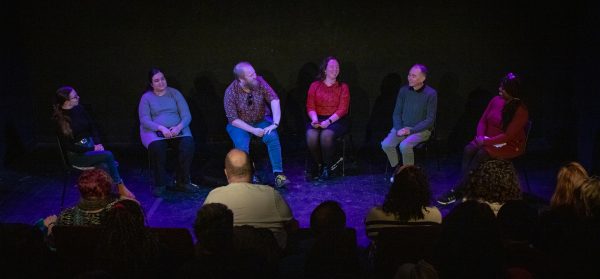 A diverse group of panel members sitting on a stage, smiling and talking to an audience.