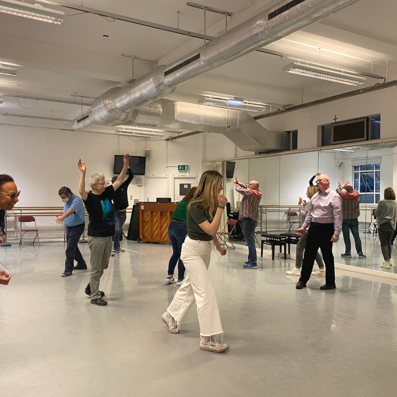 A group of participants in a drama workshop stand frozen in the brightly lit space.