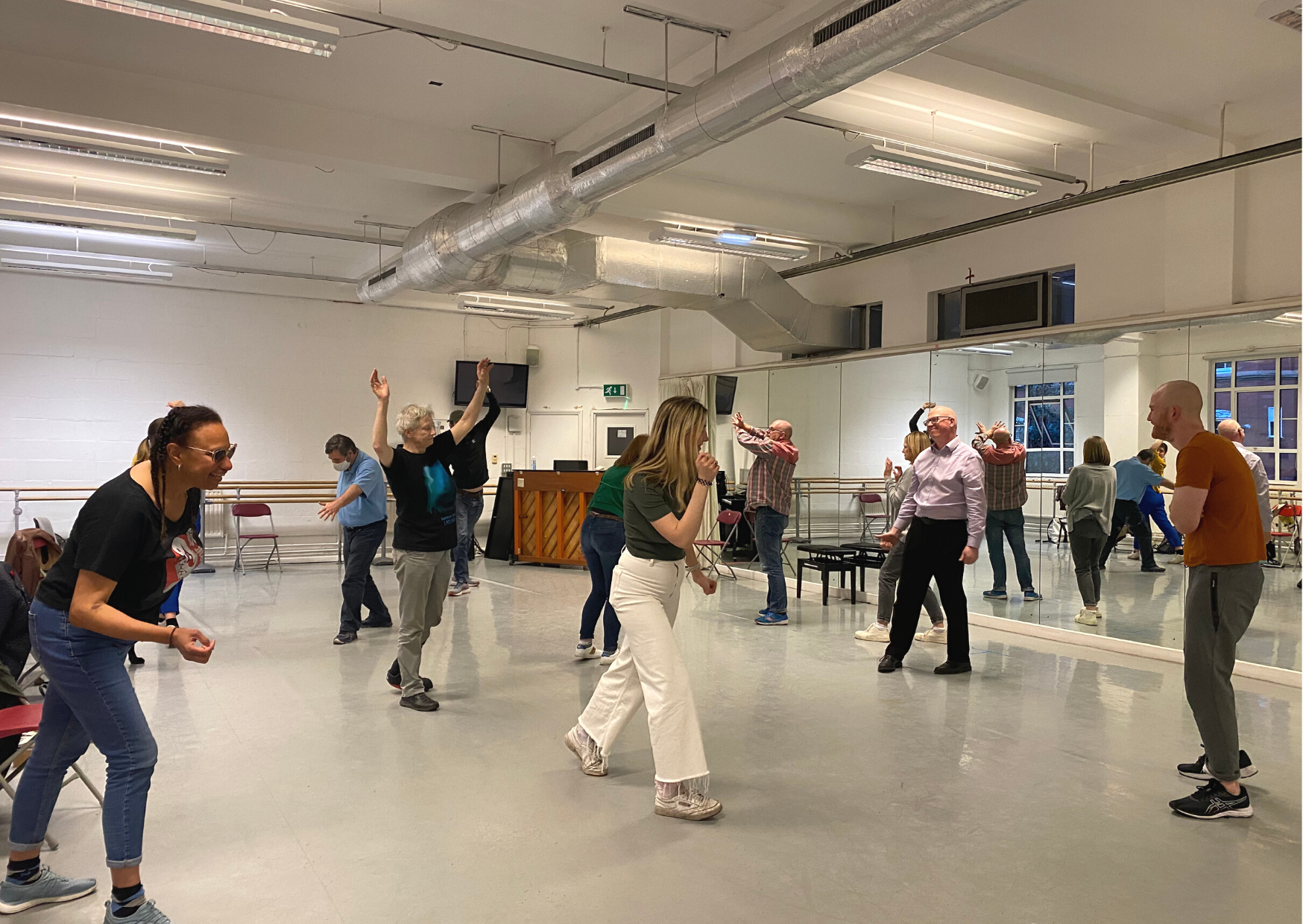 A group of participant's in a drama workshop stand frozen in the brightly lit space.