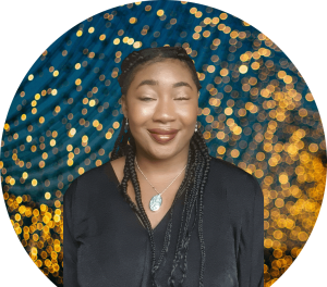 Ada, a young black woman with braided hair tied back in a half up/down style. Smiling professionally at the camera. She's wearing a blue pendant necklace with a tree of life design and a black top.