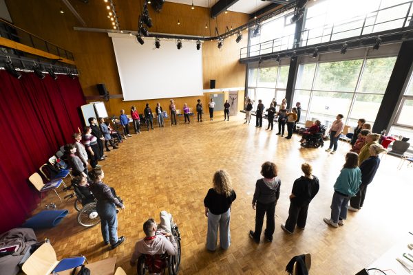 A wide angle view of a large group of participants in a circle taking part in a workshop. 