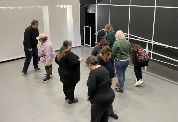 8 visually impaired people and a sighted access worker are moving around the space during a status exercise. They’re holding low body positions with their heads down.