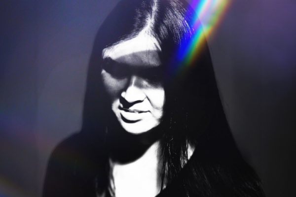 A close-up view of an east-Asian young woman's face, which is partially obscured by shadows and a bright light flare.