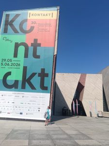 Maria, with her white cane, stands in front of the CKK Jordanki entrance with huge Kontakt conference banner.