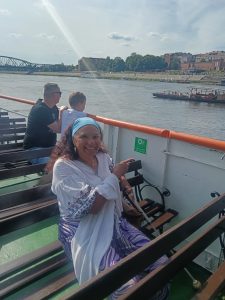Maria is sitting on the boat in the sunshine with walls of Toruń's old town behind.