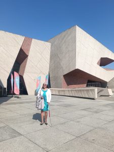 Maria smiling in the sun and standing in front of the CKK Jordanki cultural centre with unusual architecture.