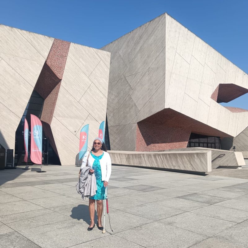 Maria standing in front of CKK Jordanki cultural centre with unusual architecture smiling in sun.